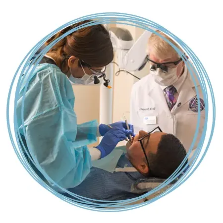 A dental student works on a patient's teeth while a professor reviews their technique